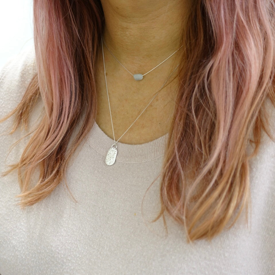 A model wearing a dainty sterling silver necklace. The pendant on the necklace has the zodiac symbol for Aries on it