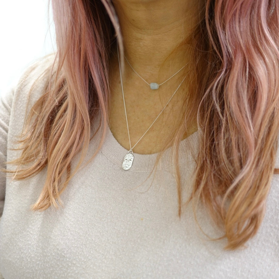 A model wearing a dainty handmade silver Moon and Dusk necklace engraved with the zodiac sign for Cancer