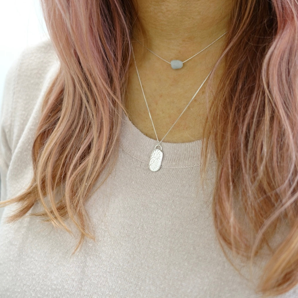A dainty Silver handmade Moon and Dusk zodiac pendant with the symbol for Leo engraved, worn by a model
