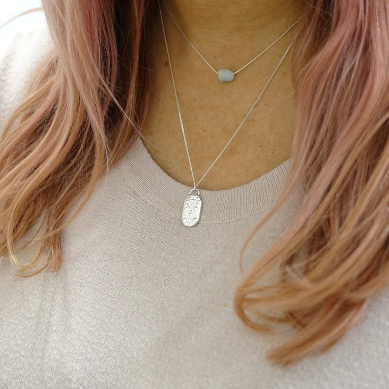 A model wearing a silver handmade necklace from Moon and Dusk. The necklace has a pendant with the zodiac symbol for Taurus on it.
