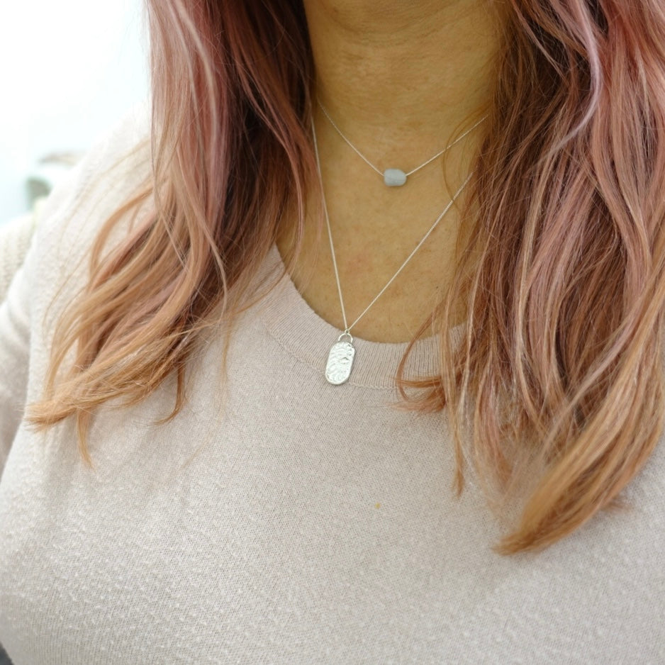 A model is wearing a dainty sterling silver Moon and Dusk necklace. The pendant has the zodiac symbol for Aquarius on it