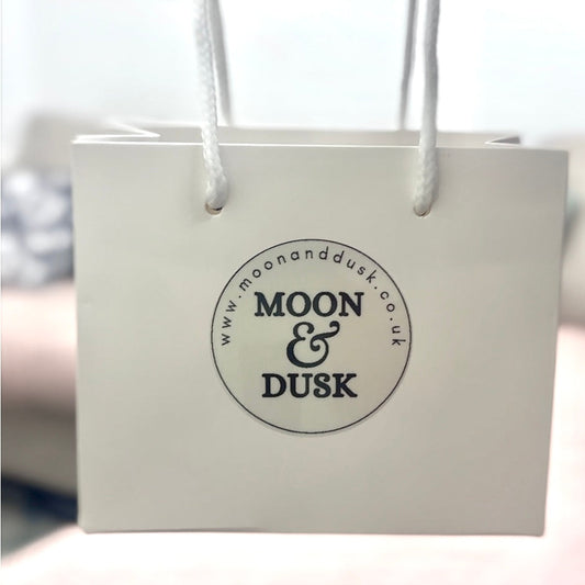 White shopping bag with 'Moon & Dusk' branding held by a hand.