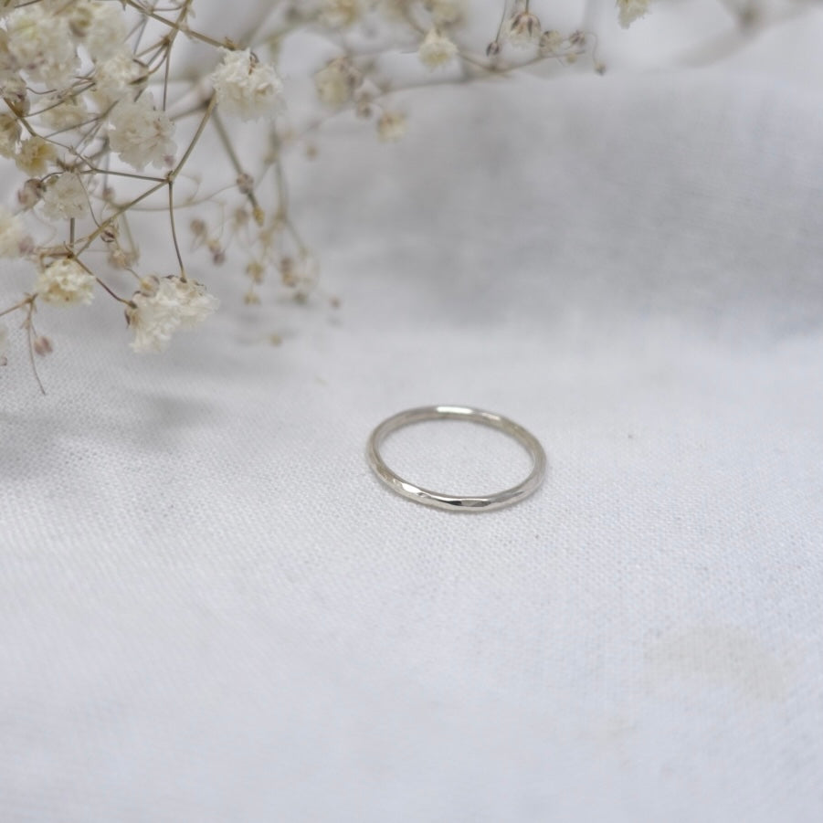 A white linen background with tiny white flowers slightly out of sight. In the centre of the picture is a sparkling Moon and Dusk silver stacking ring